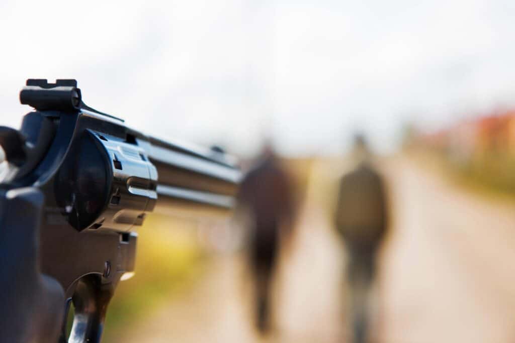 una pistola in primo piano, puntata verso due persone sullo sfondo